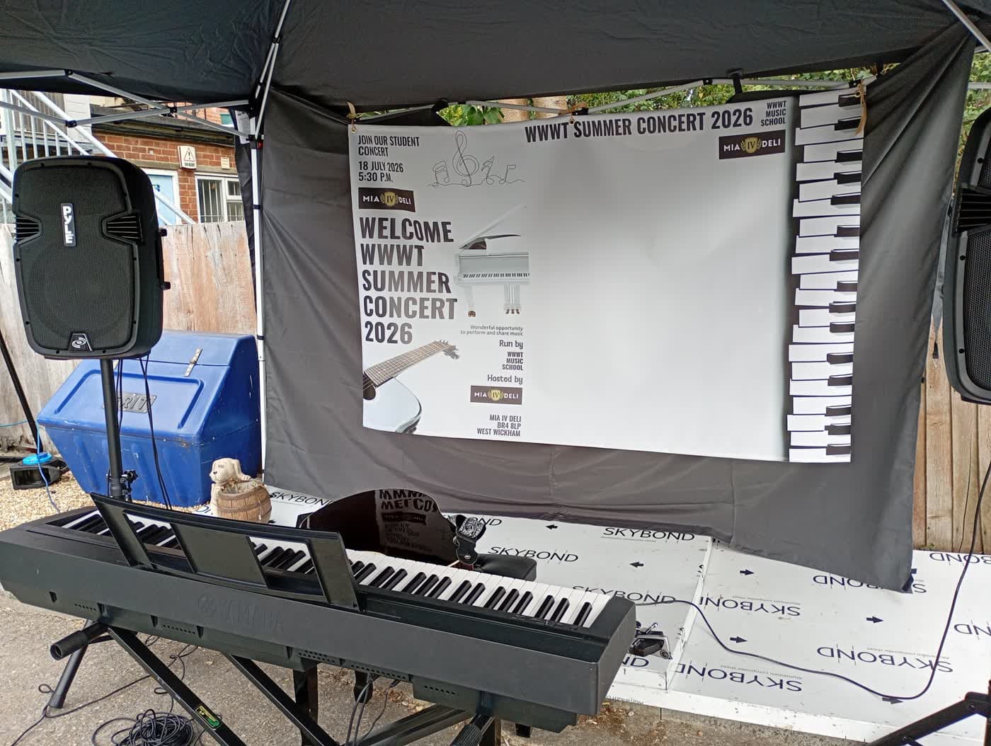 The stage set up with keyboard, guitar and the WWMT Summer Concert 2026 banner at Mia IV Deli.